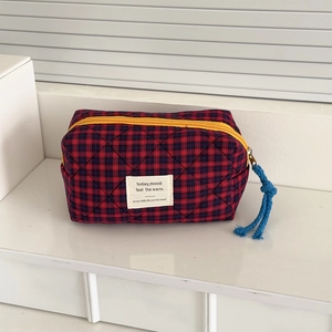 Detail of red and blue checkered quilted cosmetic bag with yellow zipper and woven label