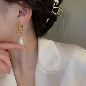 Elegant gold twisted metal earrings with baroque pearl drop worn by a female model