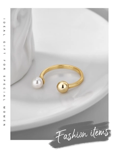 Detailed close-up of a minimalist gold ring with a white pearl and metallic ball on a tray