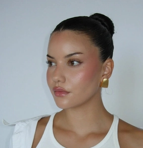 Detailed view of square gold stud earrings with vertical texture on a female model
