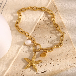 Detail view of 18K gold starfish and pearl anklet on a textured beige stone base
