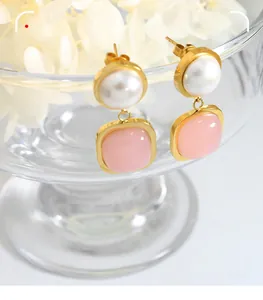 Detailed shot of gold drop earrings with a round white pearl and square pink jade stone