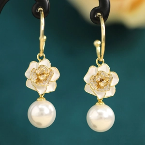 Detail of elegant gold-tone pearl drop earrings with white floral enamel and crystal studs