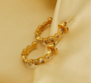 Macro shot of gold U-shaped earrings with multi-shaped crystals on champagne satin