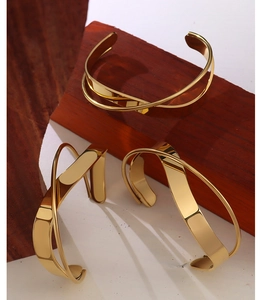 Detail of 18K gold plated stainless steel crossover bangle on dark wood props