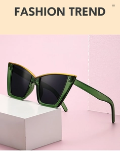 Detail of dark green cat-eye sunglasses with gold metal trim on a white geometric prop