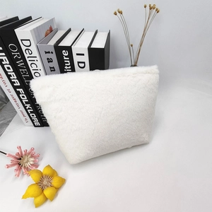 Detailed view of a white plush makeup bag with soft faux fur texture on a stack of books