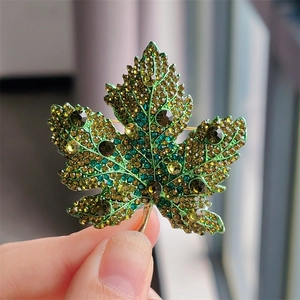 Close-up of maple leaf brooch featuring multi-colored green and gold crystals on metal base
