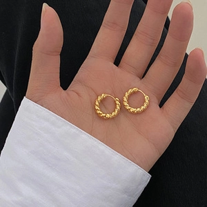 Macro shot of gold spiral twist hoop earrings in palm to show accurate size and scale