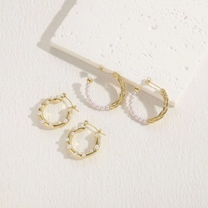 Detail of 14K gold plated earrings with freshwater pearls on a textured fabric background