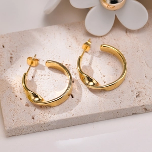 Minimalist twisted gold hoop earrings for women presented on a natural stone display