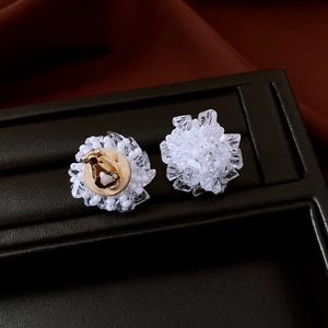 Close-up of white crystal flower clip-on earrings with gold-tone metal backing on black leather