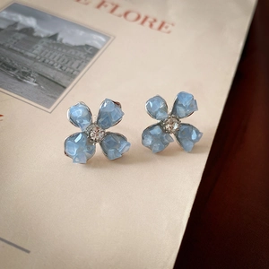 Detailed side view of silver flower stud earrings with blue resin petals on a vintage book