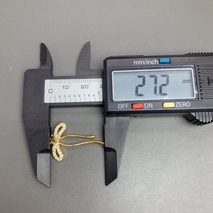 Micro-pave zircon bow pendant being measured with a digital caliper showing 27.2 mm length