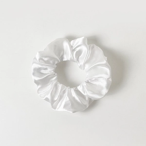 Detailed view of glossy white satin scrunchie with soft silk folds on white background
