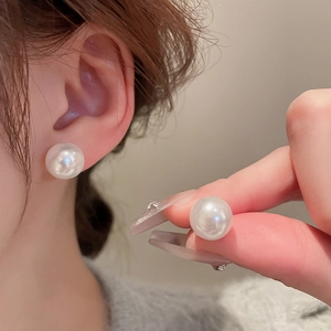 Close-up of large white round pearl earrings on ear with high luster and texture