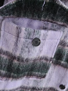Detail view of purple and grey plaid plush coat featuring pocket and button texture