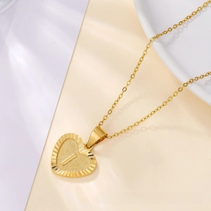 Detailed macro view of a gold heart pendant necklace with embossed letter and fine chain