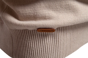 Macro shot of apricot knit sweater detail showing rib hem and leather brand label