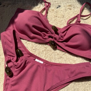 Flat lay of rose pink ribbed bikini with amber beads on soft beige carpet background