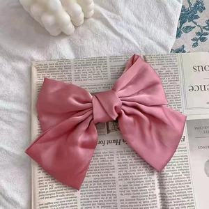 Close-up of pink satin bow hair clip with smooth texture against vintage newspaper background
