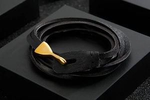 Detail of multi-layer black leather bracelet with elegant gold fishhook clasp on dark blocks