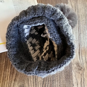 Detail of grey chunky knit beanie with faux fur pompom and jacquard wave pattern lining