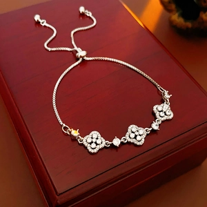 Detailed close-up of a silver four-leaf clover charm bracelet on a wooden jewelry box