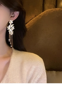 Detailed close-up of crystal butterfly tassel earrings with white flowers on silver needles