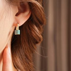Detailed close-up of a gold U-shaped earring with turquoise beaded pendant on ear