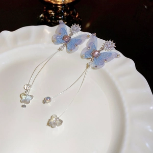 Détail de boucles d'oreilles papillon bleu clair avec pompons, perles et cristaux
