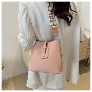Pink bucket bag with lychee texture and logo strap worn by a model in a casual blazer