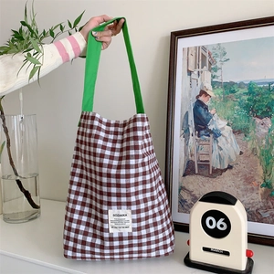 Détail d'un sac cabas en toile à carreaux marron et blanc avec des anses vertes