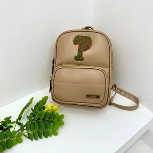 Detail of beige PU backpack featuring green letter embroidery and metal logo plate