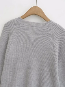 Detail of gray knit sweater featuring a round neckline and raw edge button accents