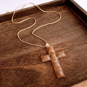 Detailed macro view of a large resin cross pendant on a gold twisted chain over wood