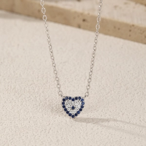 S925 sterling silver heart necklace with blue evil eye stones on beige background
