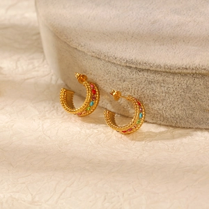 Detail of gold C-shaped twisted hoop earrings with multi-color rhinestones on beige background