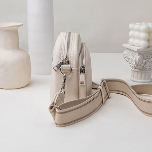 Chic beige crossbody bag with pebbled leather texture and decorative wide shoulder strap