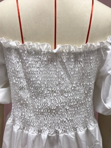 Detail of smocked white off-shoulder dress with red ribbon and ruffled neckline trim
