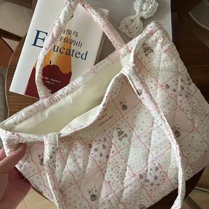 Detail of quilted floral tote bag with cute rabbit pattern and small woven label on wood