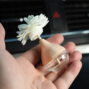 Hand holding car glass aroma diffuser bottle with wooden lid and white flower diffuser