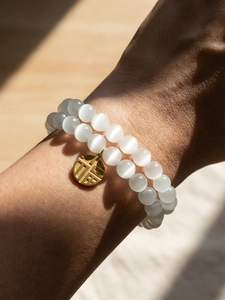 Detail of double-layer white cat-eye stone bead bracelet with a gold Fu pendant