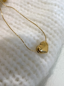 Detailed view of a gold heart pendant necklace on a white knitted fabric background