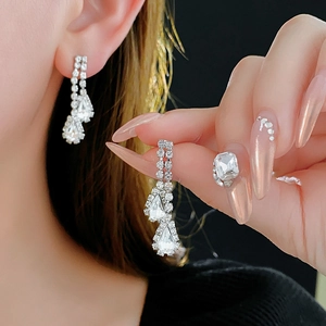 Detail view of elegant silver teardrop earrings with square diamonds on a female model