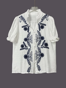 Detail of blue floral embroidery and ruffle collar on a white cotton blouse
