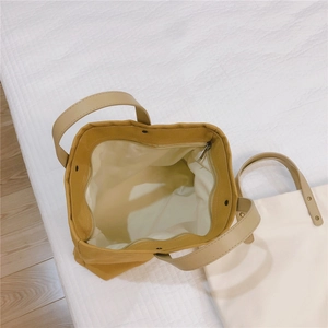 Detail of mustard yellow and off-white canvas tote bags with leather handles and zip closure
