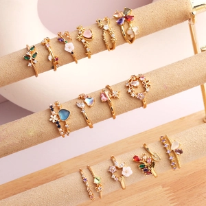 Detailed close-up of gold-plated rings with floral and heart zircon stones on a beige stand