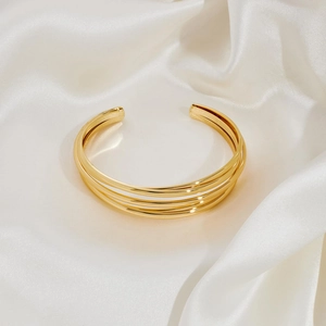 Minimalist 18K gold multilayer open bangle on elegant white silk background