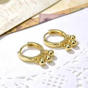 Minimalist gold hoop earrings with three dangling metal beads on white lace background